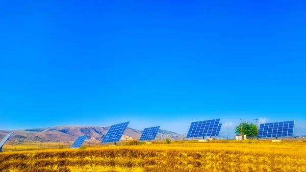 Solar panels for electricity generation in a field with a hill covered in colourful autumn trees in background on a sunny day