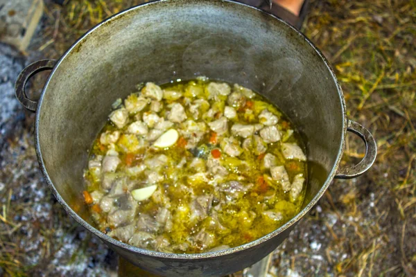 kettle with food camping. camping food - barbeque outdoor in summer camp. Hot big wok pan full of fried tasty potato on the fire in the forest. Fried potatoes on a fire in a forest in a pan.