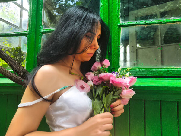 The beautiful girl in the hands of a pink bouquet of different flowers. Behind a background from green wooden boards