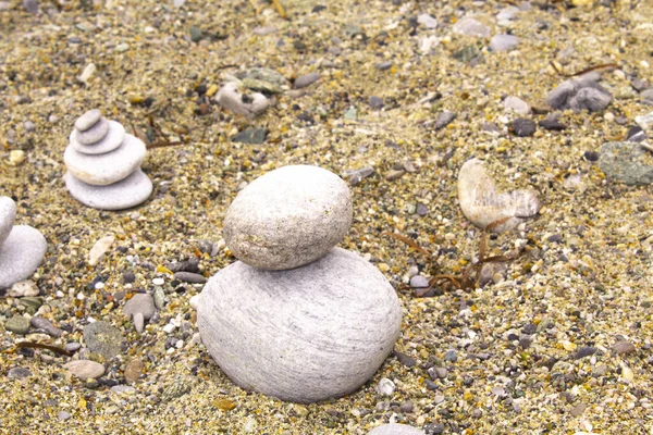 zen stone on sand, pebble art , small flat stones carefully placed together, conceptually, to resemble a pyramid form