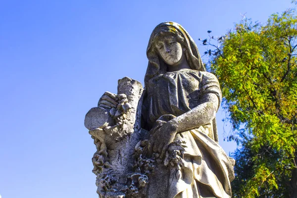 跪着的天使雕像 双手交叉在蓝天和有十字架背景的墓碑上 — 图库照片