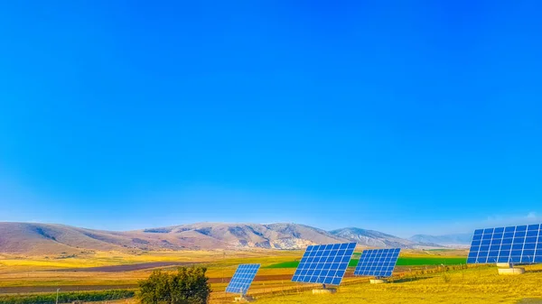 Solar panels for electricity generation in a field with a hill covered in colourful autumn trees in background on a sunny day