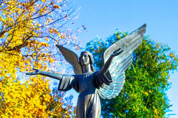 跪着的天使雕像 双手交叉在蓝天和有十字架背景的墓碑上 — 图库照片