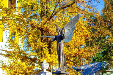 Kolları mavi gökyüzüne ve mezar taşına bağlı diz çökmüş haçlı bir melek heykeli.