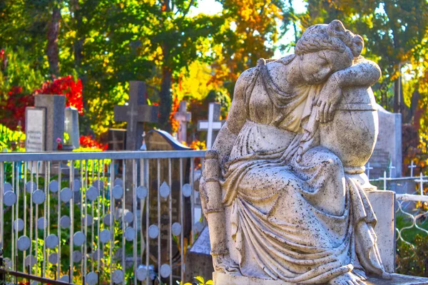 statue of kneeling angel with arms crossed against blue sky and cemetery headstone with crucifix background