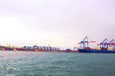 Odessa, Karadeniz 'deki akşam limanında portallar. Denize yanaşmış ağır bir yük gemisi. Arka planda konut ve ticari binalar bulunmaktadır.