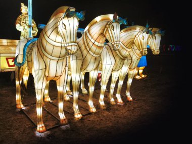 Küçük ışıklarla aydınlatılmış beyaz bir at modeli. Hayvan halka açık bir bahçede. Gece vakti Çin ipeğinden yapılmış at feneri..