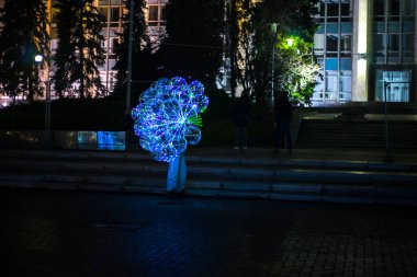 Gece boyunca sokakta elinde çelenklerle balon tutan bir adam..