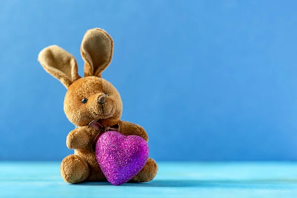 Toy brown bunny with a pink heart. On a classic blue color background.