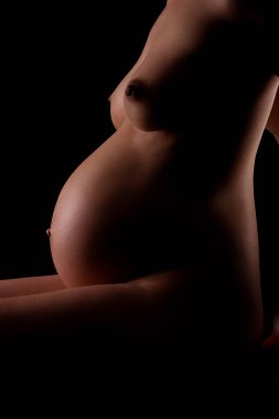 pregnant woman with a naked torso on a black background clipart