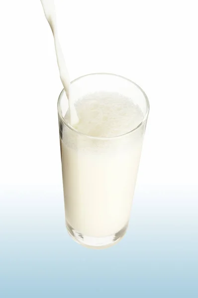 在白色背景上的杯子里倒入牛奶 — 图库照片