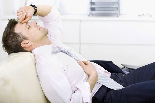 一个中年生意人躺在办公室的沙发上 疲倦的样子 闭着眼睛 明亮的背景 — 图库照片