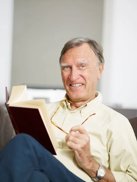 Senior Man Reading Book Home Looking Camera Copy Space — Stock Photo, Image