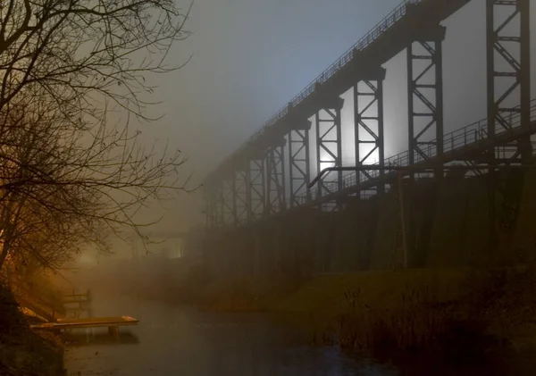 小川のほとりでとても夢のようなロマンチックな小さな橋が 別の工場を囲むスポットライトに照らされ 寒さと輝きを表しています — ストック写真
