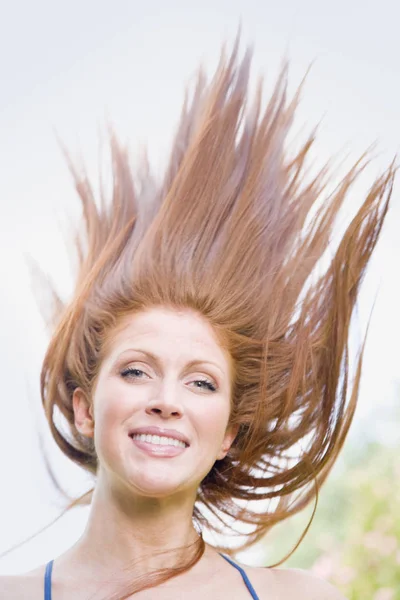 風に吹かれた髪の若い女性の屋外のイメージ 彼女はカメラを見て笑っており 頭と肩が見える 縦枠のショット — ストック写真
