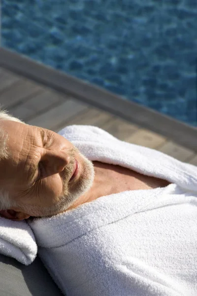 Old man lying on a lounge chair beside a swimming pool