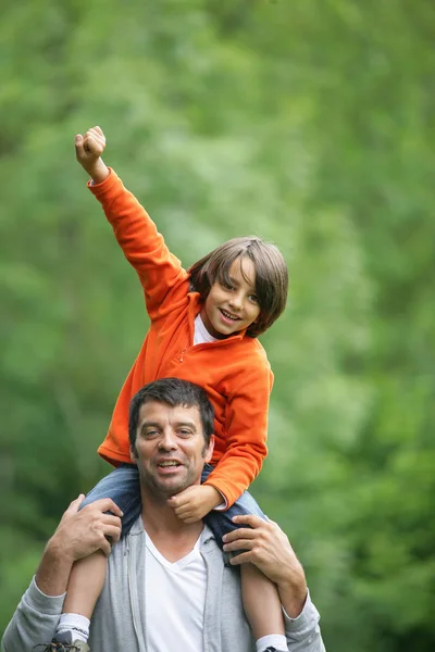 Portrait of a smiling man carrying a small boy on his shoulders in the country