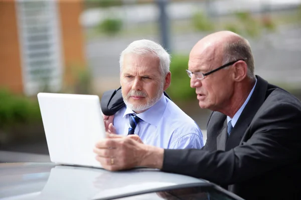 Portrait of older men in suits in front of a laptop computer placed on the roof