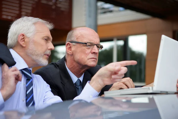 Portrait of older men in suits in front of a laptop computer placed on the roof