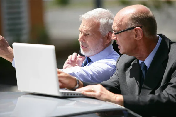 Portrait of older men in suits in front of a laptop computer placed on the roof