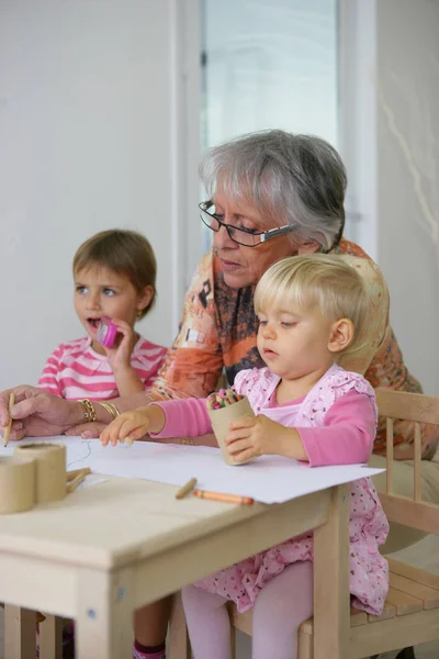 Kobieta Senior Kolorowanki Prawie Dwie Małe Dziewczynki Siedzi Przy Biurku — Zdjęcie stockowe