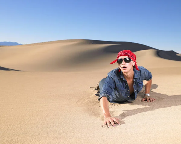 砂の中を這う赤いバンダナを着たサングラスの若い男 水平射撃 — ストック写真