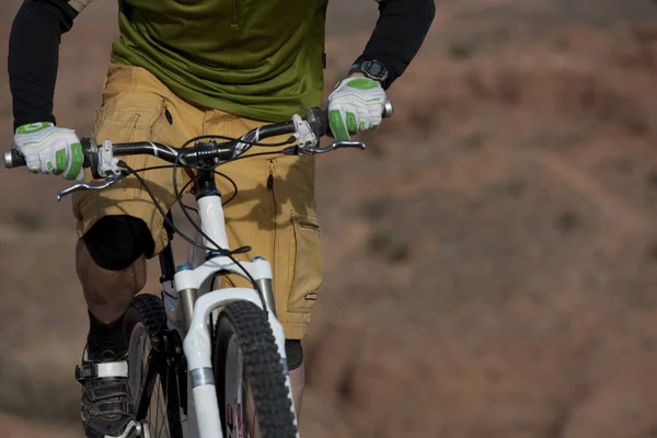 The torso of a man riding a mountain bike in a desert landscape. Horizontal shot.