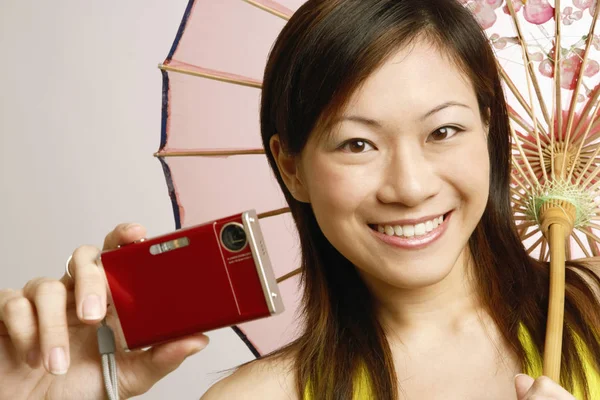Portrait of a young woman holding a digital camera and a parasol