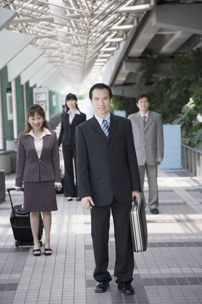 Businessman walking and holding his suitcase with three business executives in the background