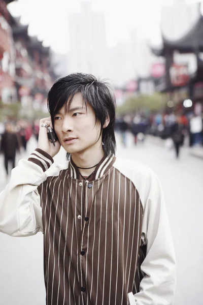 Close-up of a young man using a mobile phone with his hands in his pockets