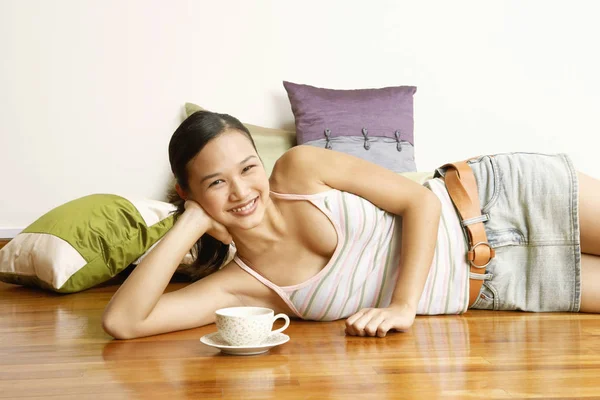 Portrait of a young woman lying on the floor with a tea cup in front of her