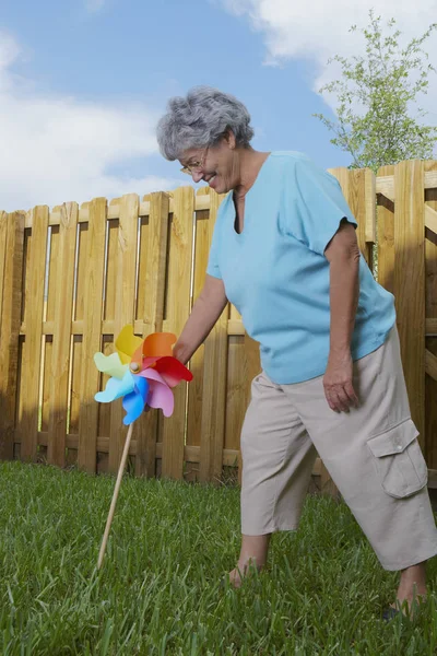 Side profile of a senior woman fixing a pinwheel in a lawn and smiling