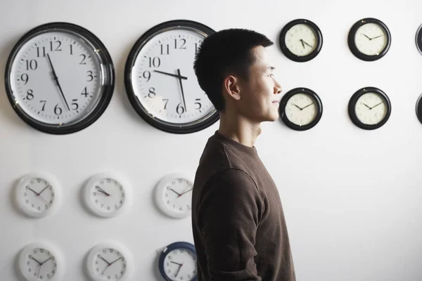 Side profile of a businessman standing in front of clocks on the wall