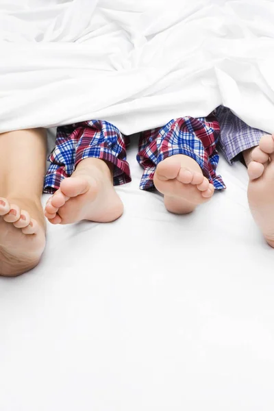 Close-up of a couple\'s feet with their child on the bed