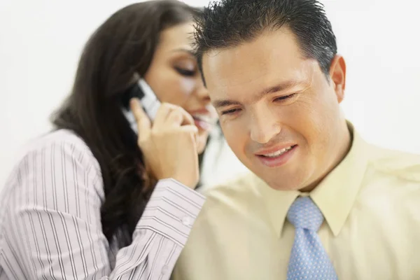 Close-up of a businesswoman talking on a flip phone and whispering to a businessman