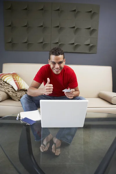 Portrait of a young man sitting in front of a laptop and showing thumbs up