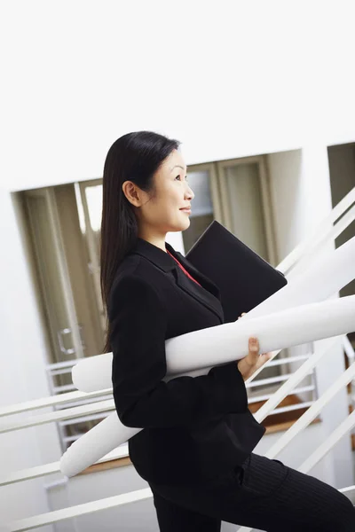 Side profile of a businesswoman carrying rolled charts and smiling