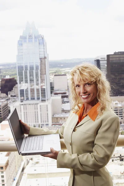 Portrait of a businesswoman holding a laptop with buildings in the background