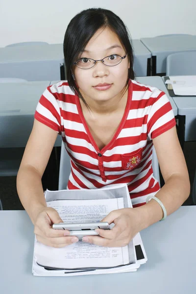 Portrait of a young woman sitting in the classroom and holding a personal data assistant