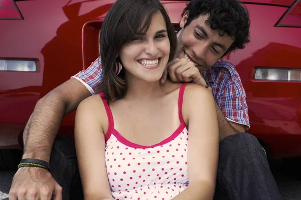 Close-up of a young couple sitting in front of a car