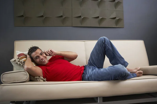Side profile of a young man talking on a mobile phone and lying on a couch
