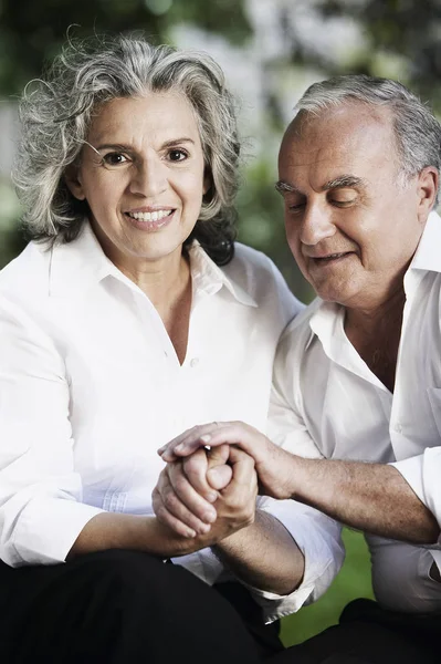 Portrait of a senior woman smiling with a senior man holding her hands