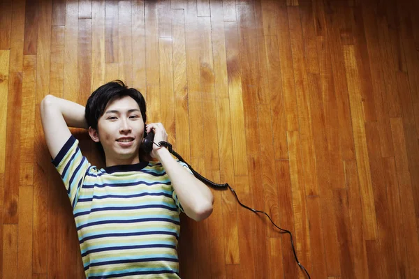 Portrait of a young man talking on the telephone and lying on a hardwood floor