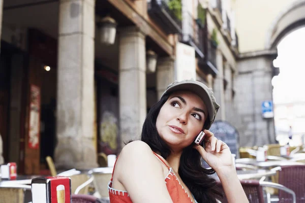 Side profile of a mid adult woman sitting at a sidewalk cafe and talking on a mobile phone