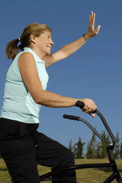 Side Profile of a senior woman cycling and waving her hand