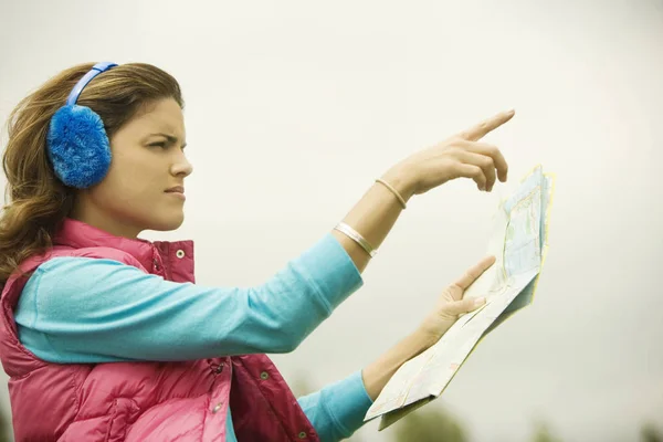 Side profile of a young woman holding a map and pointing forward
