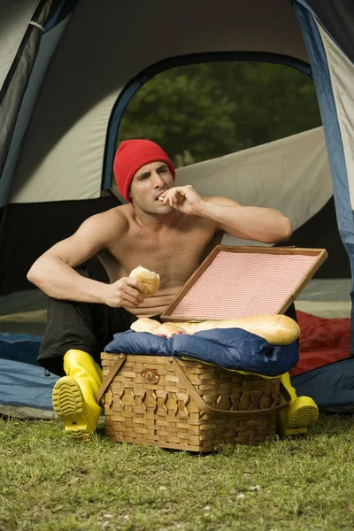 Mid adult man eating a bun sitting in a dome tent