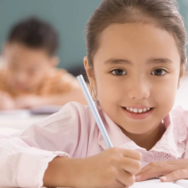 Portrait of a schoolgirl writing on a notebook with a pencil and smiling