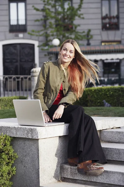 Young woman sitting on a ledge and using a laptop