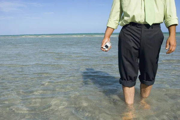 Mid section view of a man holding a flip phone in water